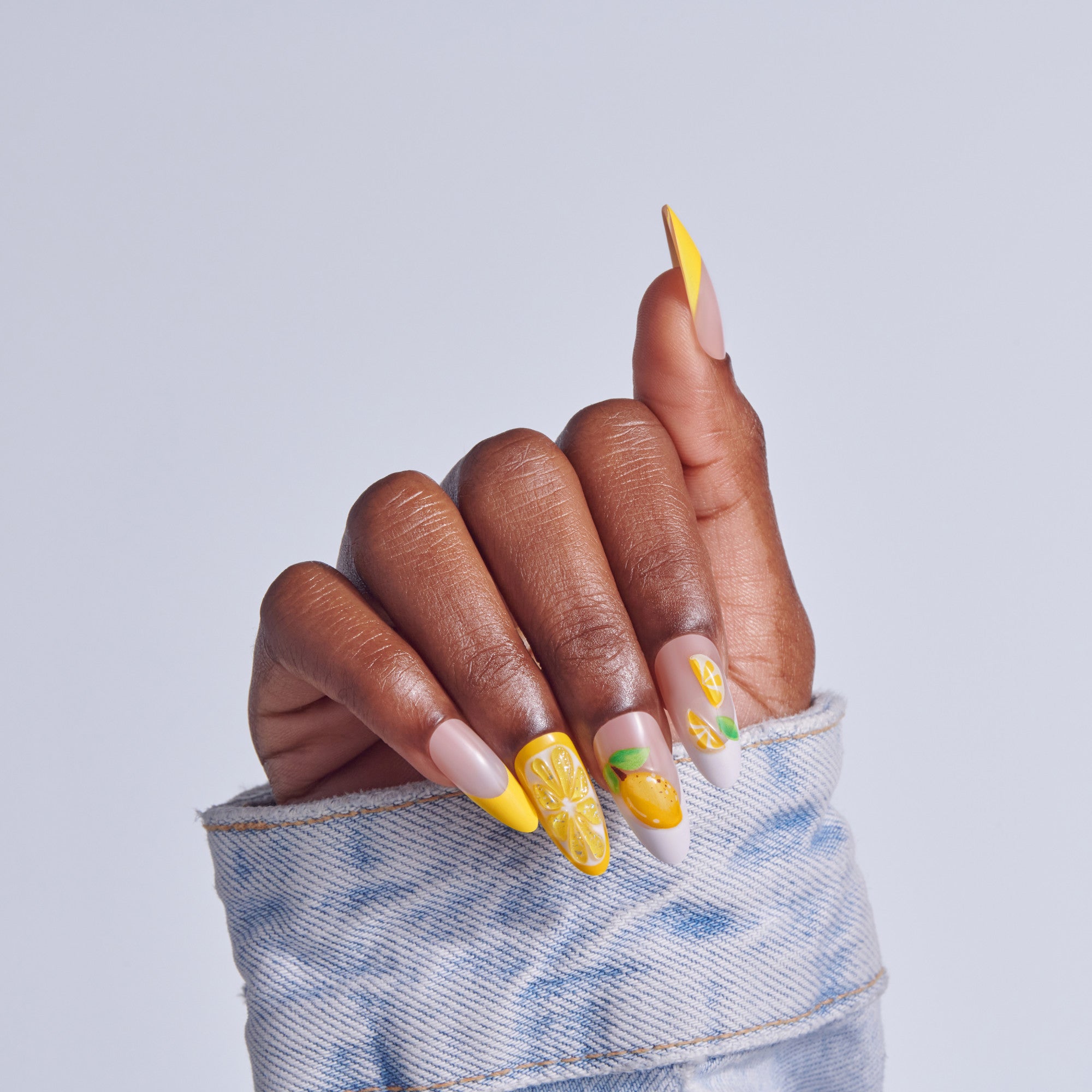 Hand displaying yellow lemon nail art design with nude base on almond nails.