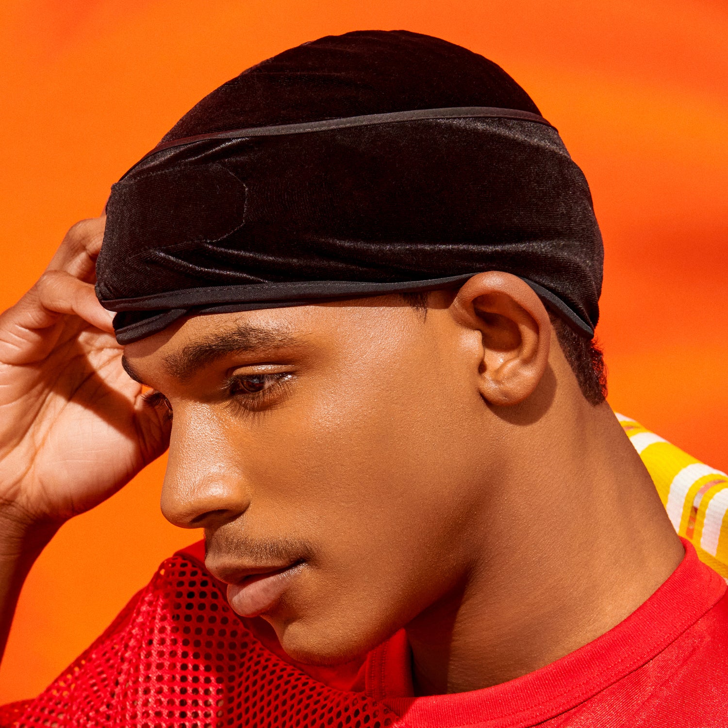Close-up of a person wearing a black luxe velvet durag against an orange background, highlighting smooth texture and comfortable fit.