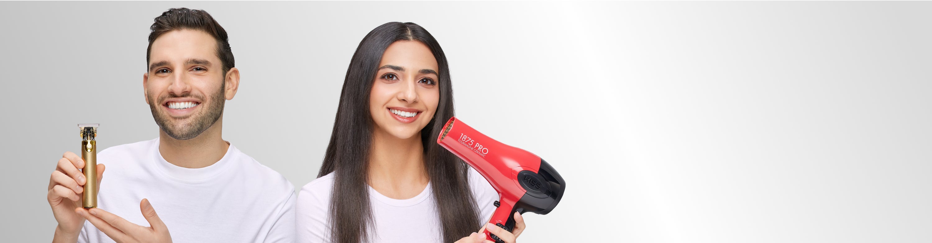 Man holding trimmer and woman holding red KISS PRO hair dryer, both smiling against gray background.