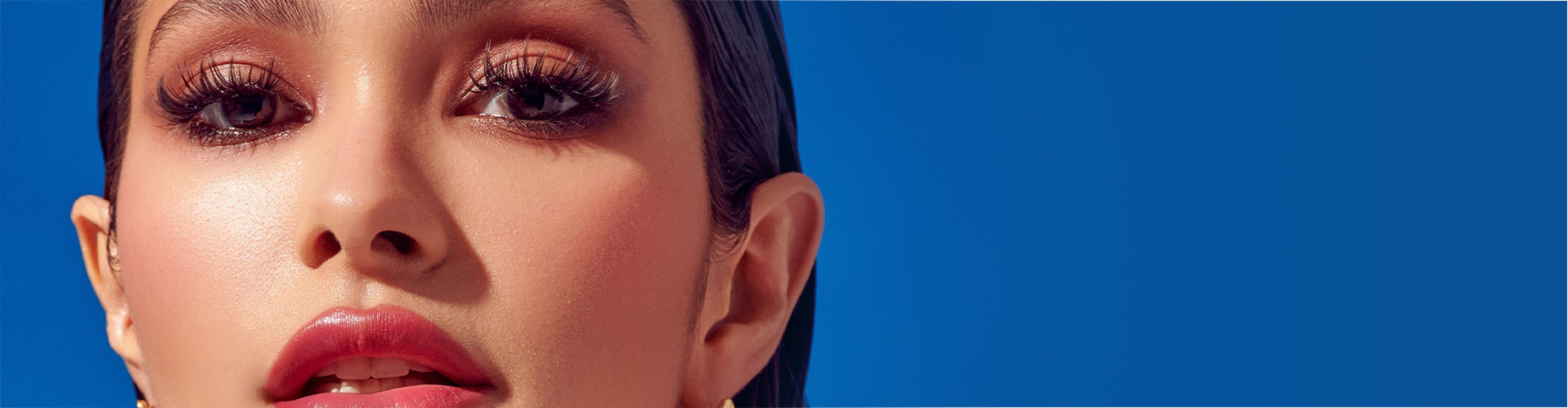 Woman wearing KISS lashes against blue background, makeup closeup