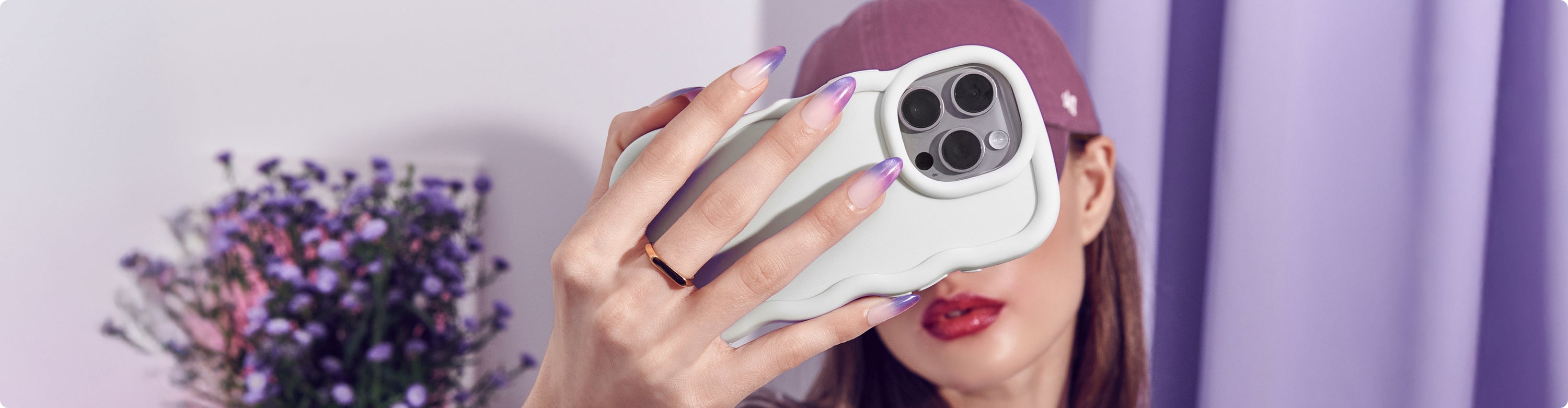 Person holding white iPhone 14 Pro case with purple manicure and flowers in background