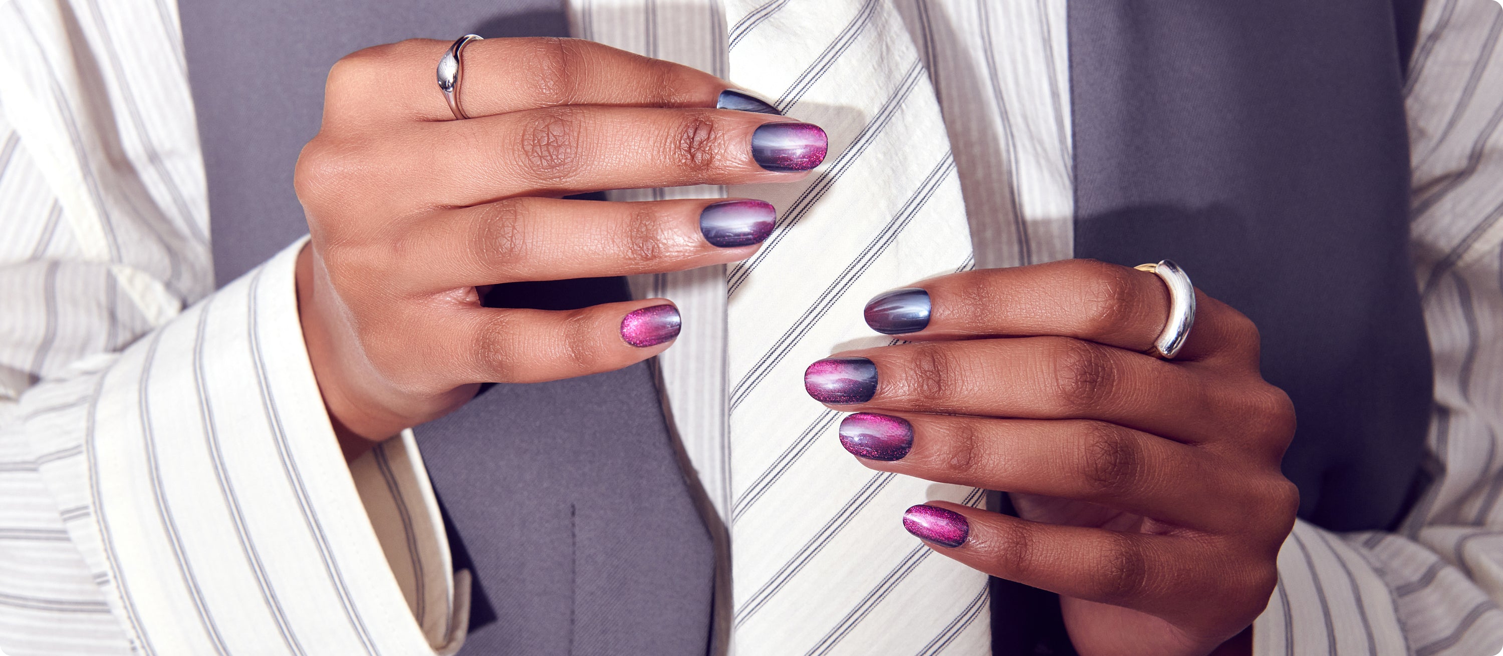 Person wearing striped white shirt displaying metallic purple ombré manicure with rings
