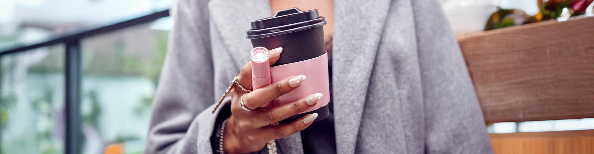 Woman holding KISS lipstick and coffee cup outdoors