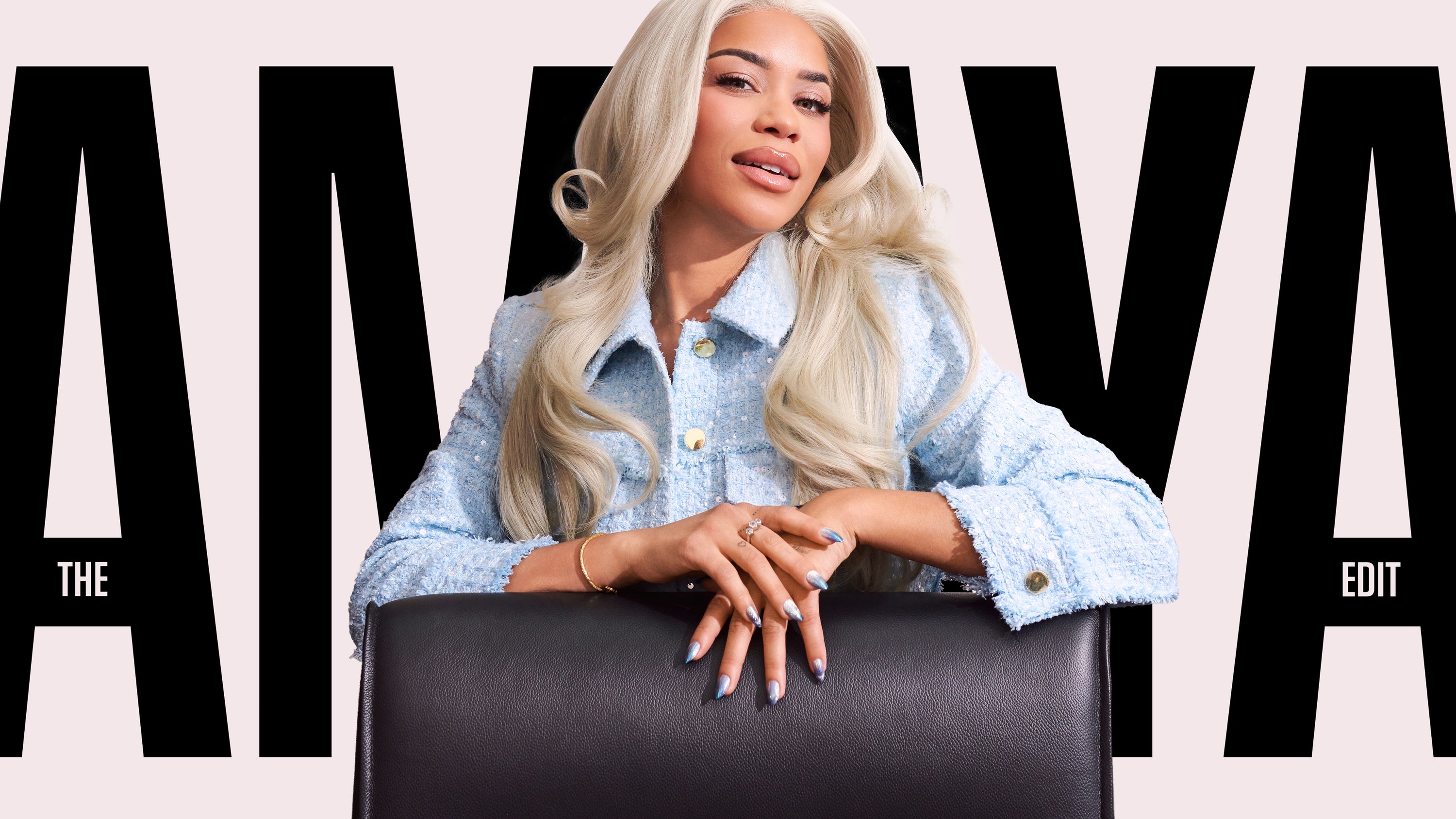 Person with long blonde hair sitting on a black chair against a pink background with 'AMAYA' branding.