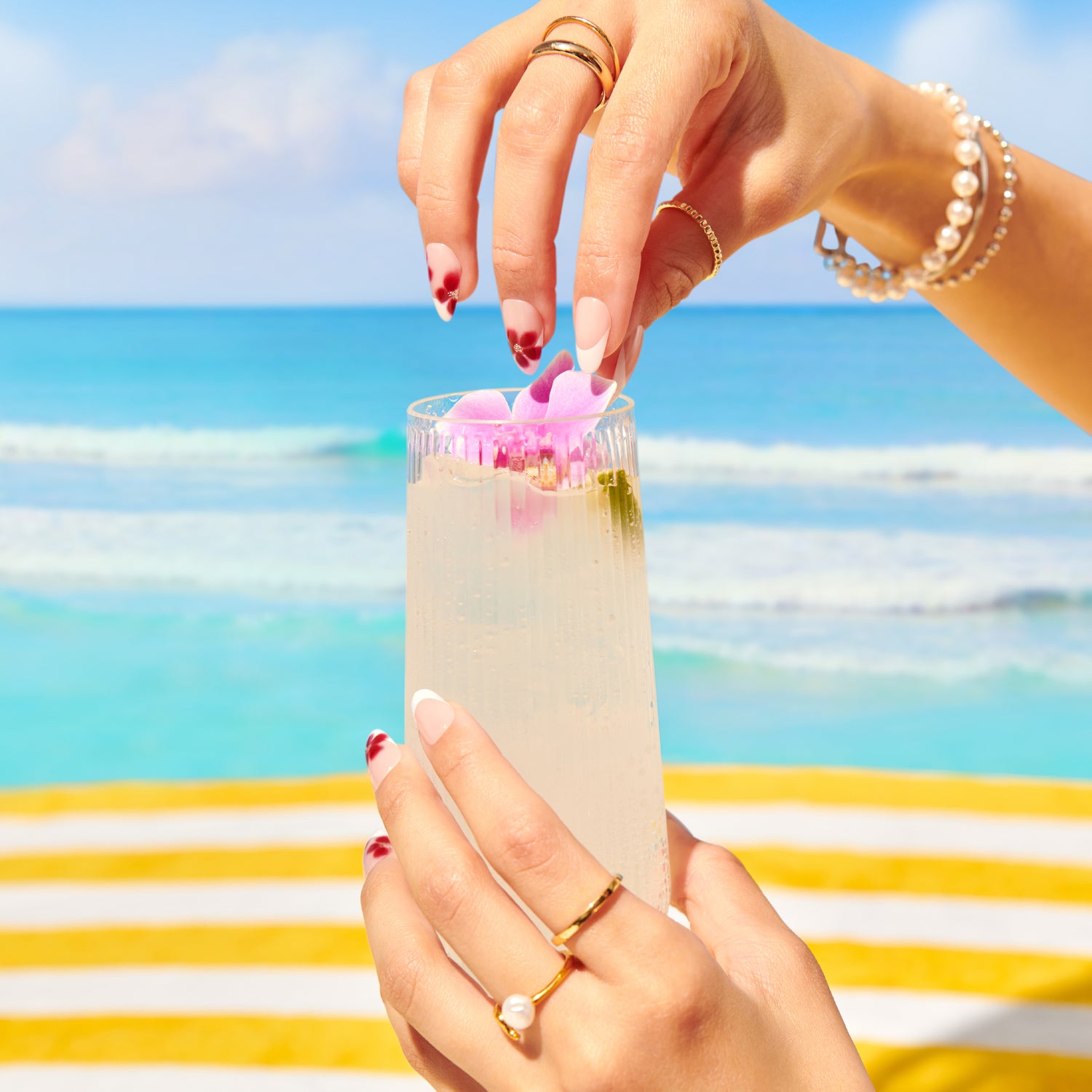 Person holding a cocktail with flowers against a beach background