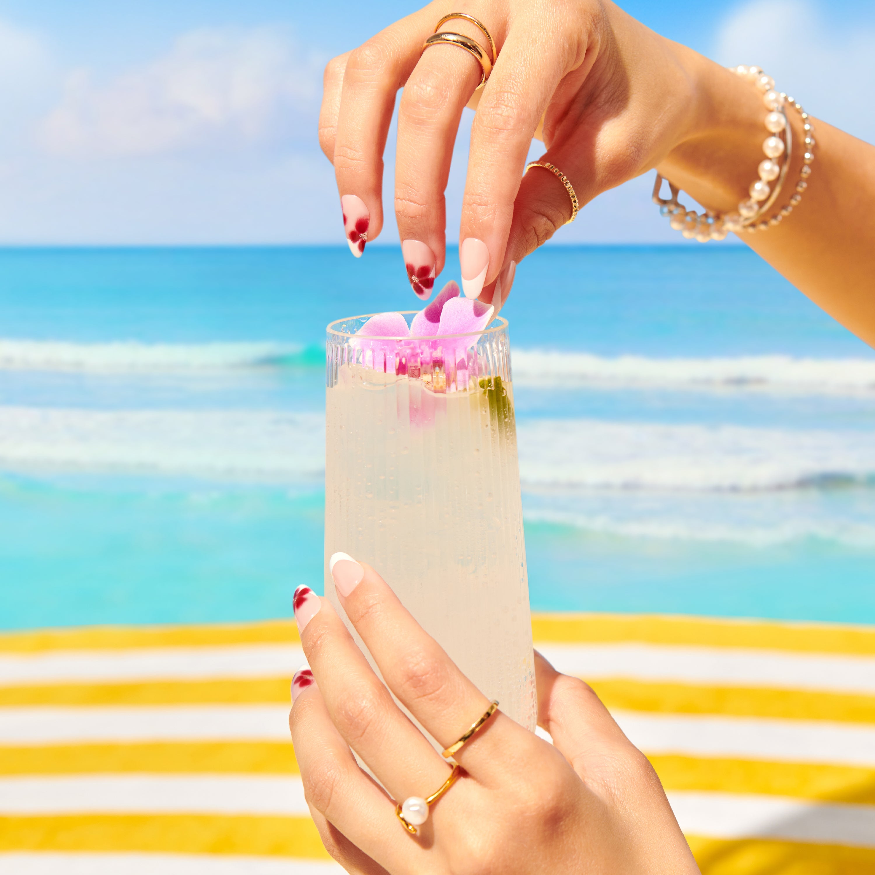 Person holding a cocktail with flowers against a beach background