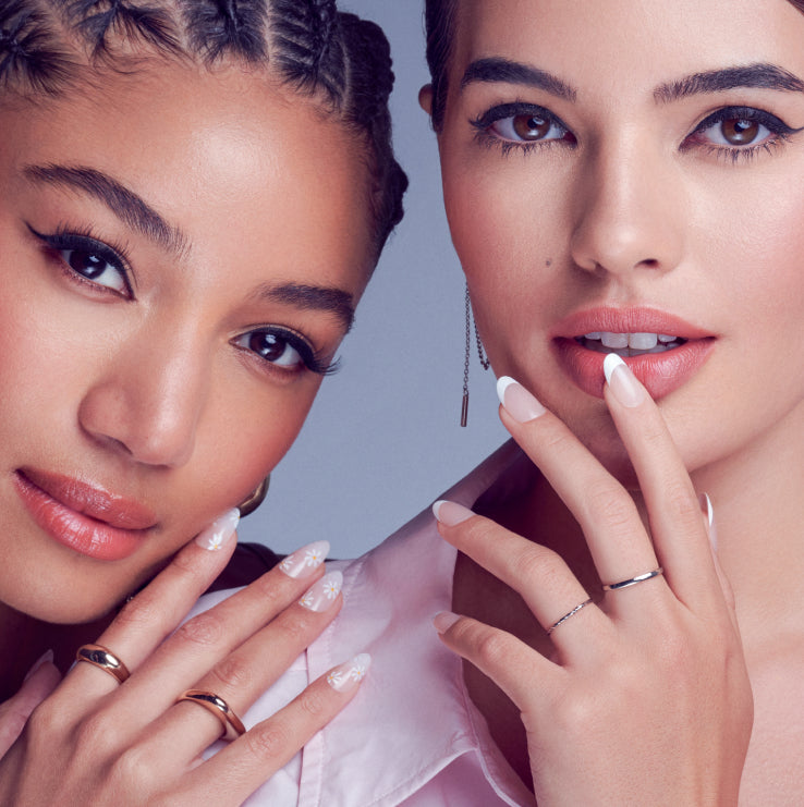 Two women displaying manicured nails with rings against blue background.