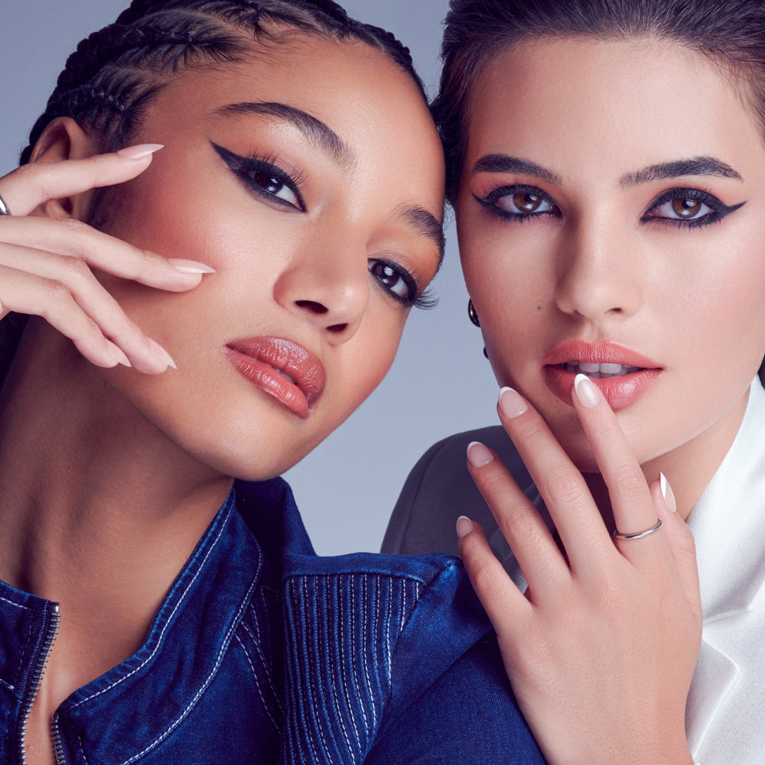 Two women showcasing bold eyeliner and nude lipstick makeup looks against blue background.