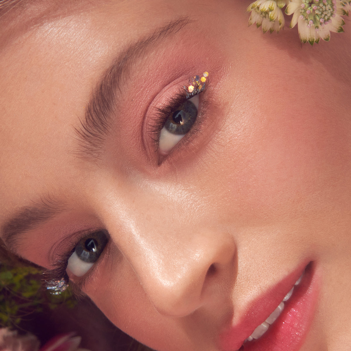 Close-up beauty shot: model with burgundy eyeshadow, rhinestone accents, and coral-pink lips.