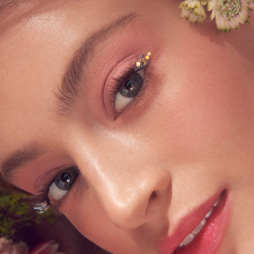 Close-up beauty shot: model with burgundy eyeshadow, rhinestone accents, and coral-pink lips.