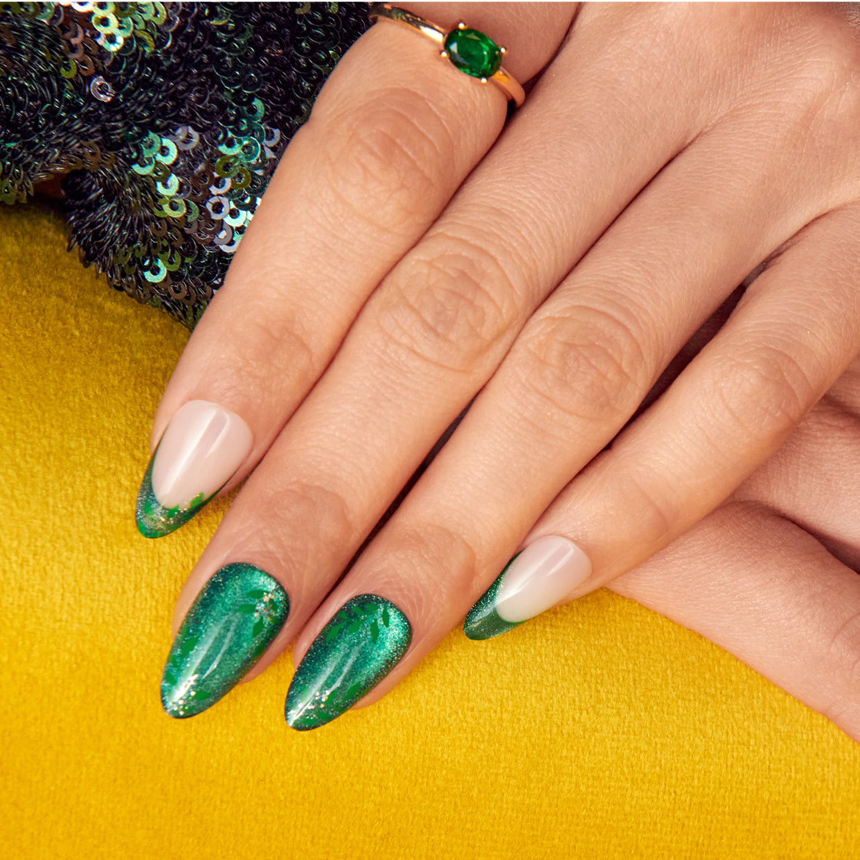 Green glitter and nude nail design with emerald ring on yellow background.