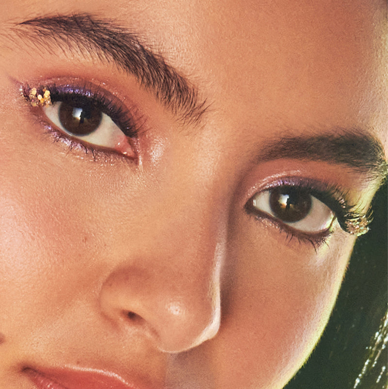 Close-up of model's face with warm eyeshadow, gold eyeliner accents, and defined brows.
