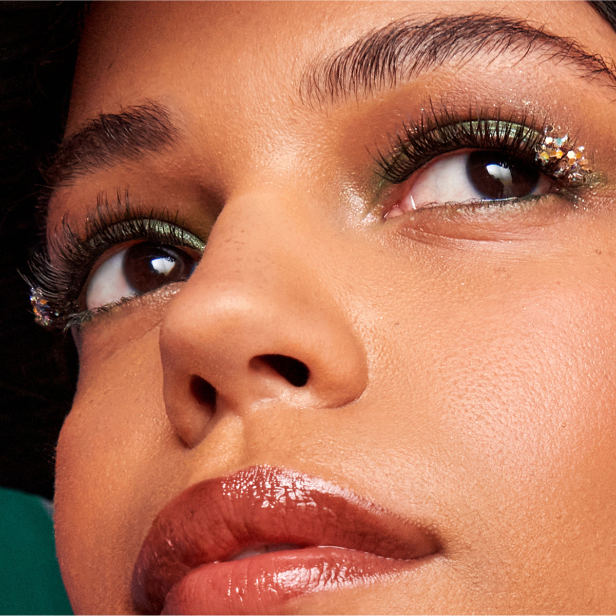 Close-up of model with gold eyeshadow, glitter accents, full lashes, and deep red lips.