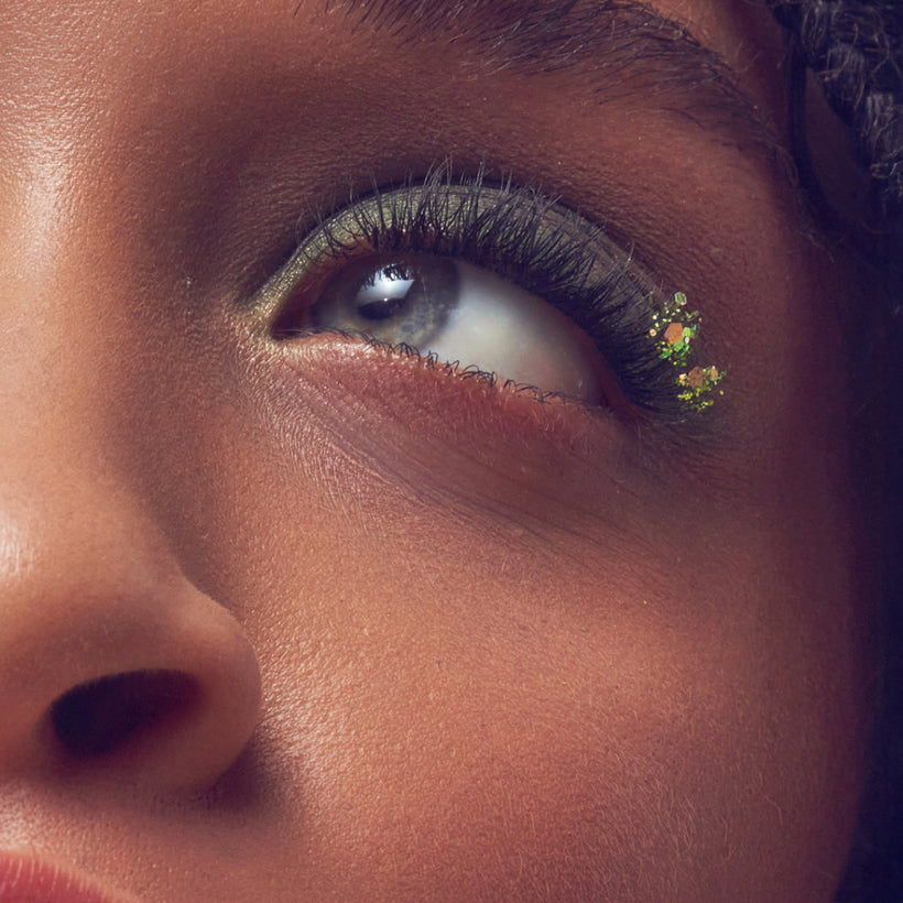 Close-up of eye with gold eyeshadow, black eyeliner, and decorative gold glitter accent on lower lash line.