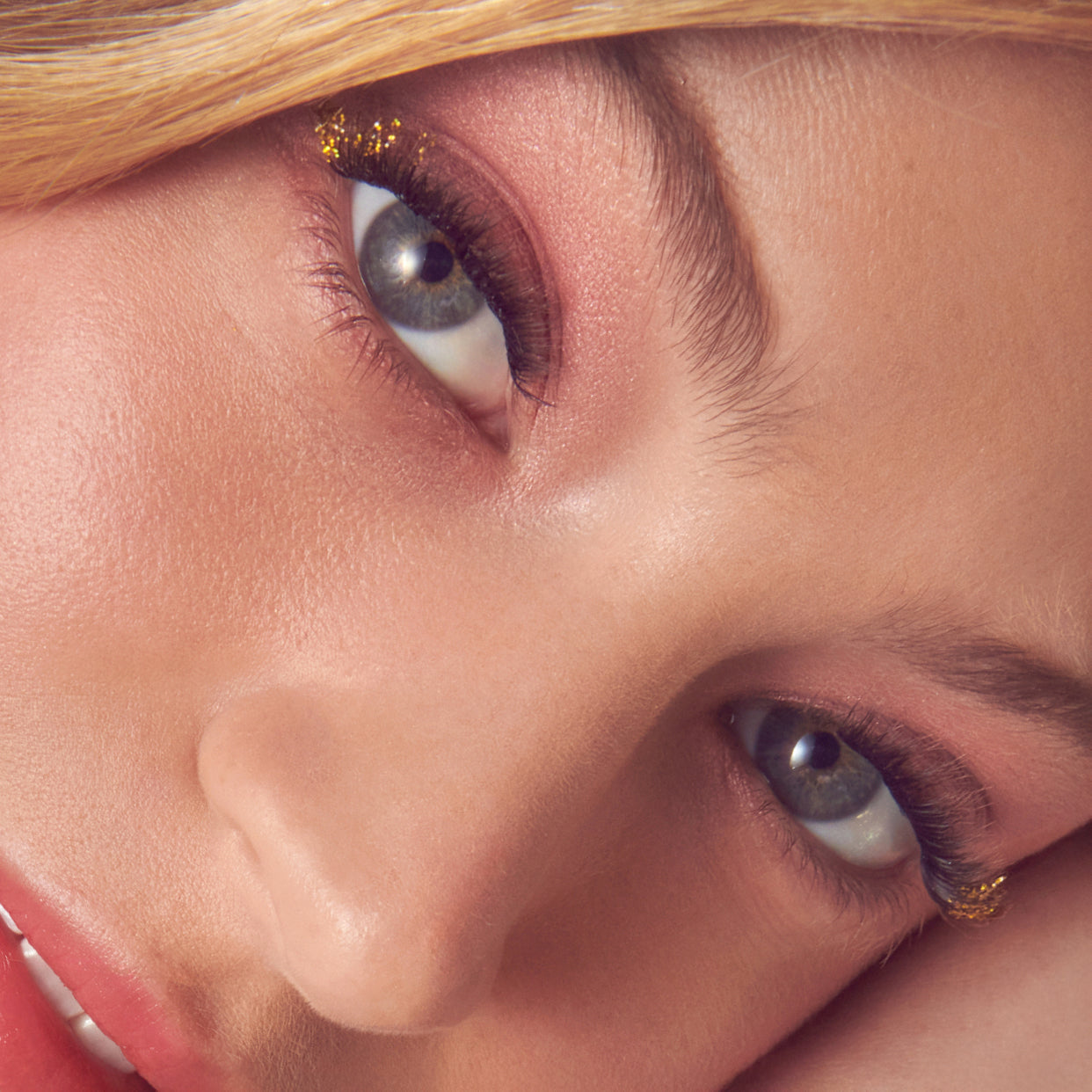 Close-up of woman's face with gold-accented eye makeup and full lashes.