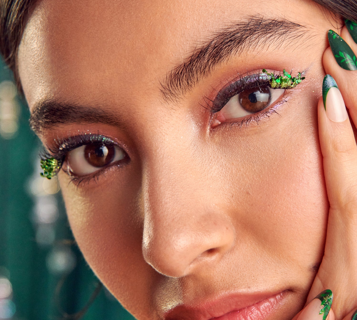 Close-up of woman's face with dark eyeshadow and green glitter eyeliner and nails.