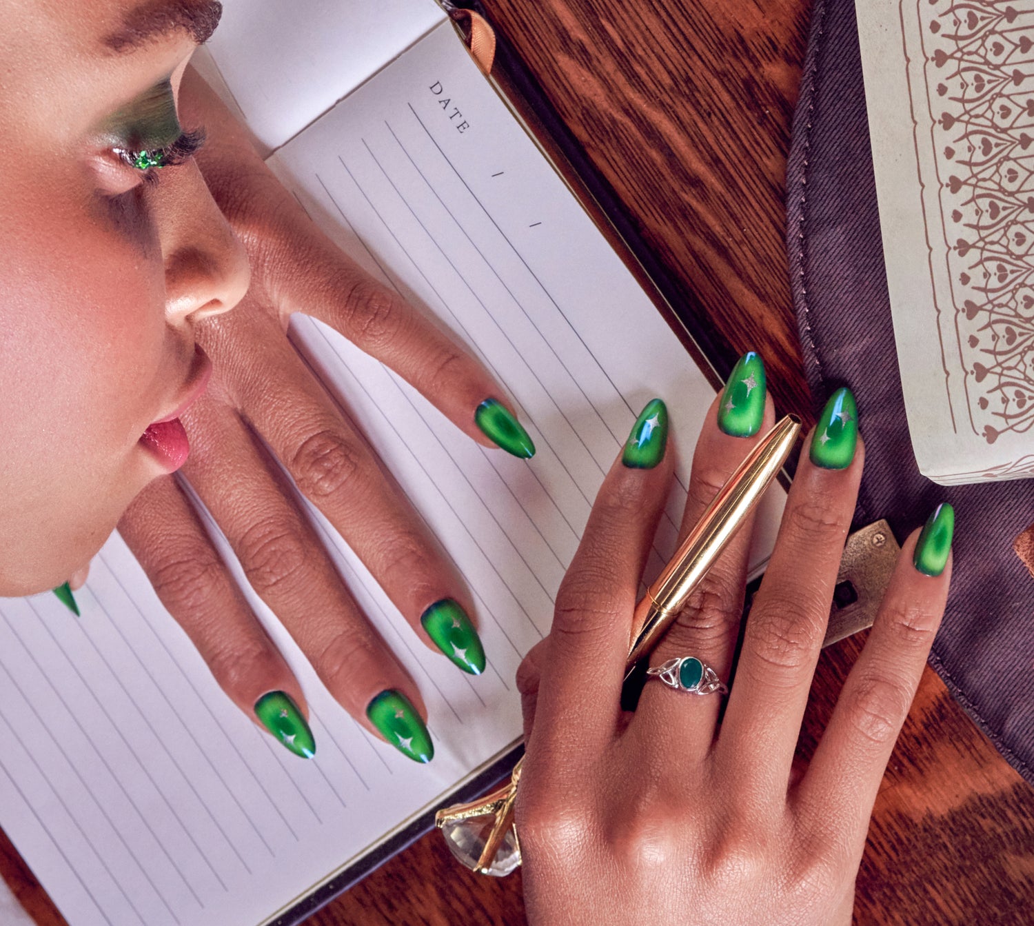 Person with green ombré stiletto nails holding notebook with "DATE" text visible.