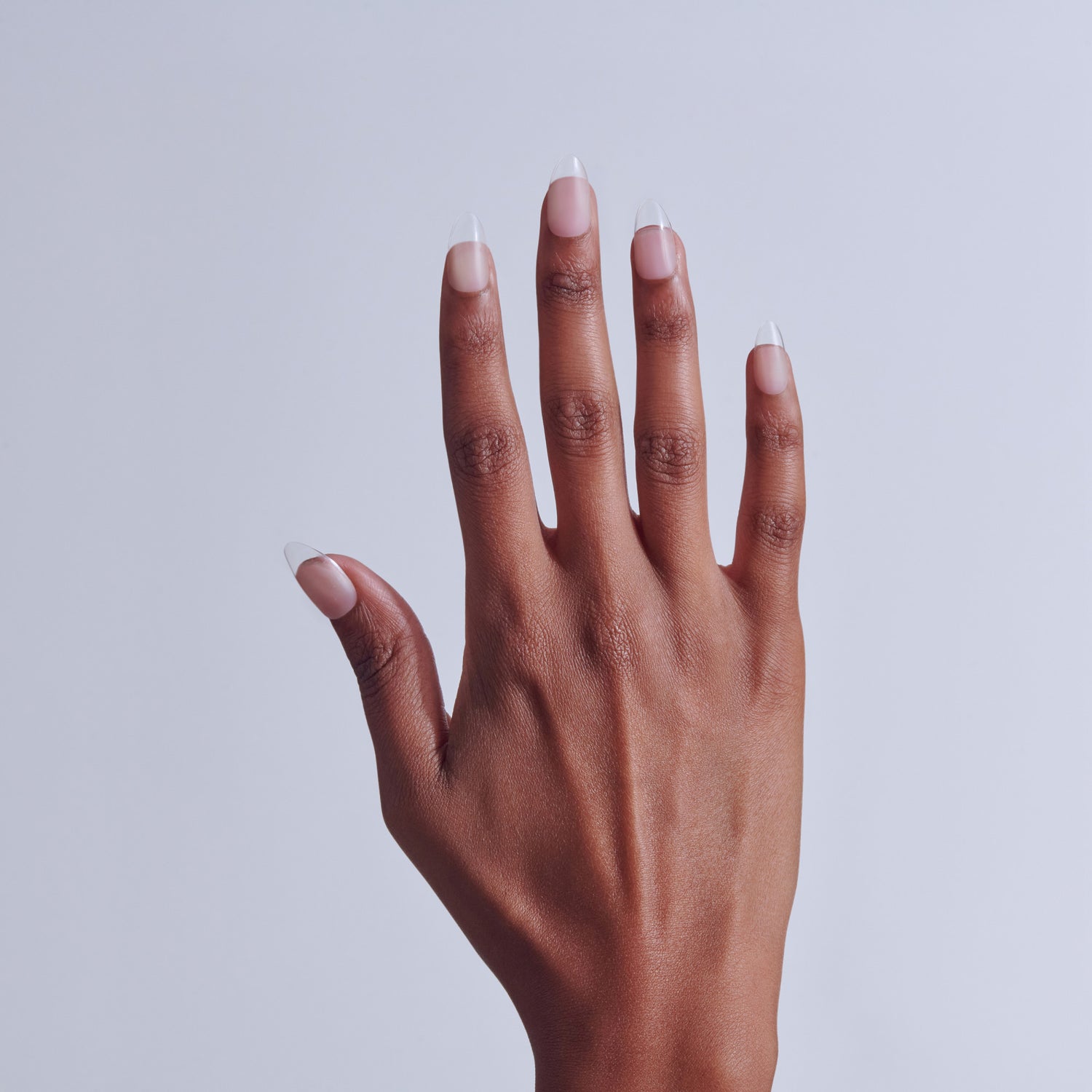 Hand with white-tipped French manicure nails against light gray background.