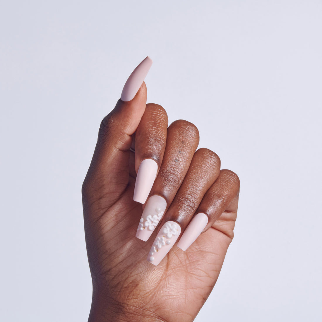 Hand with pale pink coffin-shaped nails, some adorned with pearl beads, against white background.