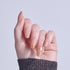 Manicured hand with nude and gold nail art design against light background.