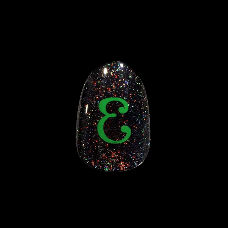Black glittery press-on nail with multicolored sparkles and a bright green stylized letter \