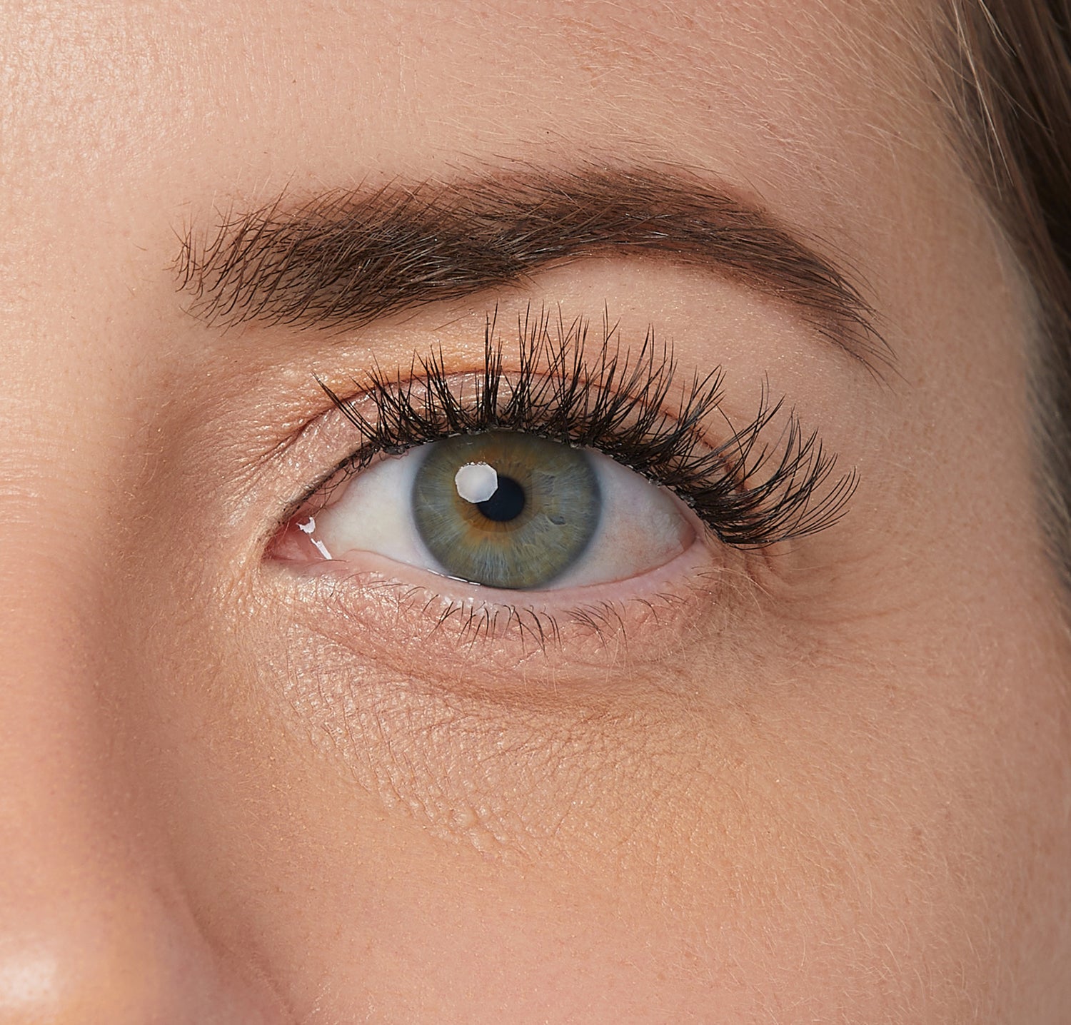 Close-up of a green eye with long, curled false eyelashes and well-groomed dark eyebrow on natural skin tone.