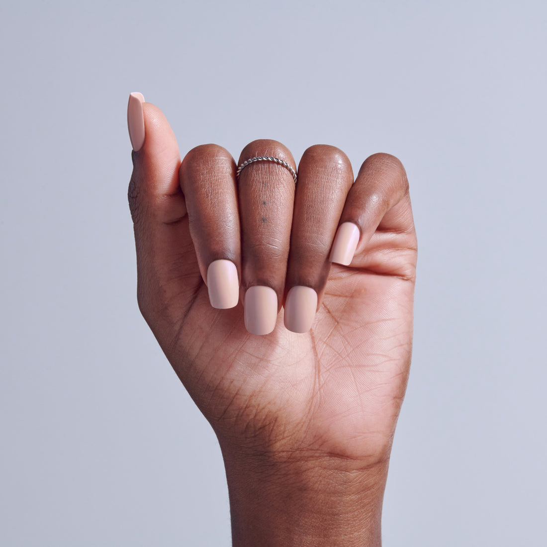 Hand with pink and nude manicure and delicate silver ring against gray background.