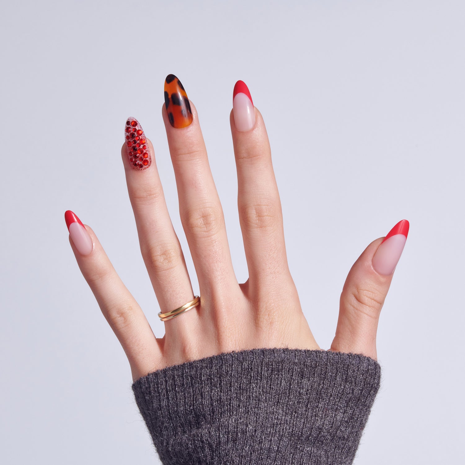 Hand displaying five nail art designs: red glitter, tortoiseshell, red ombre, red tip, and red tip variants.