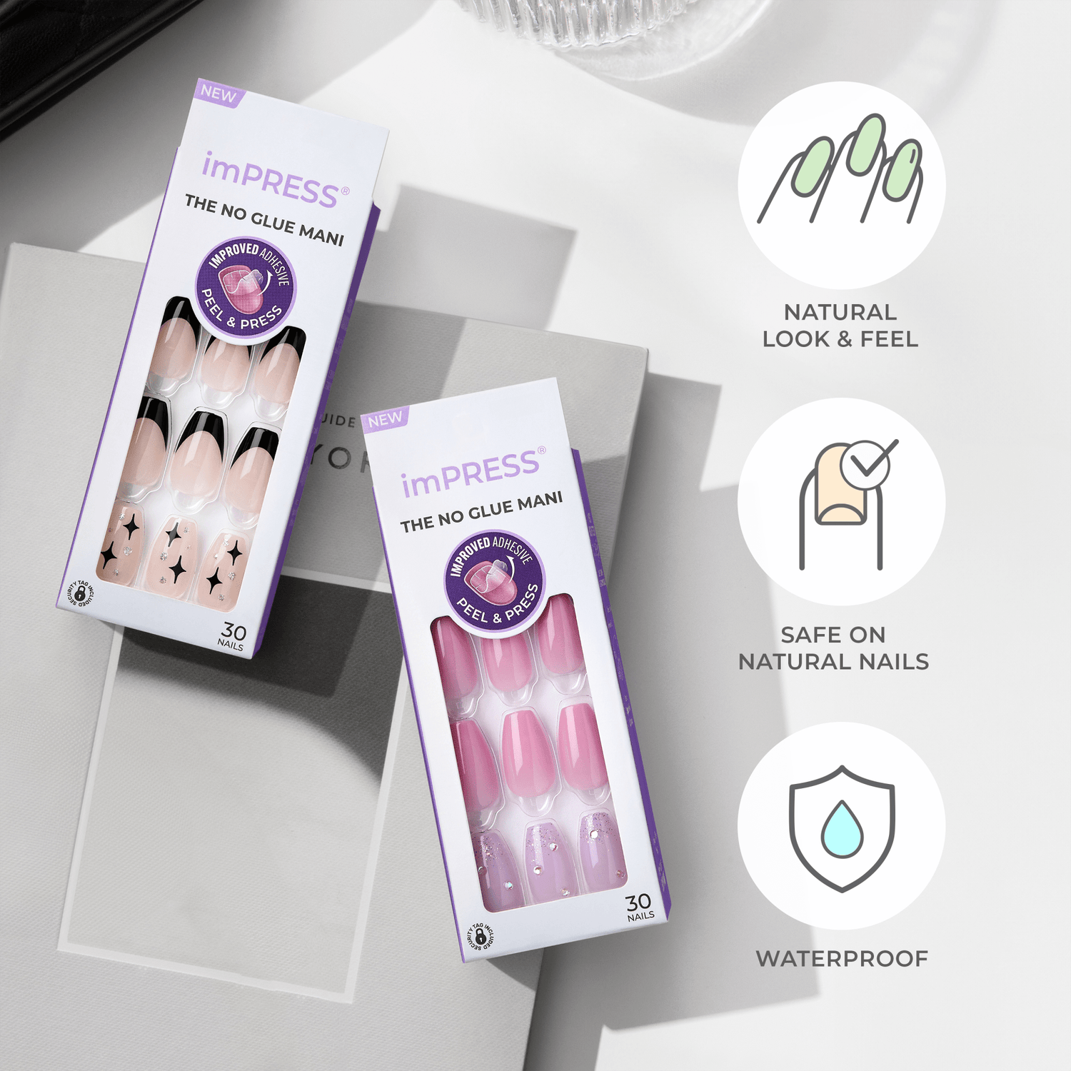 Two imPRESS Design Press On Nails packages displayed on a table with bright lighting. One package shows nude nails with black tips and star designs; the other shows pink nails with rhinestones and glitter.