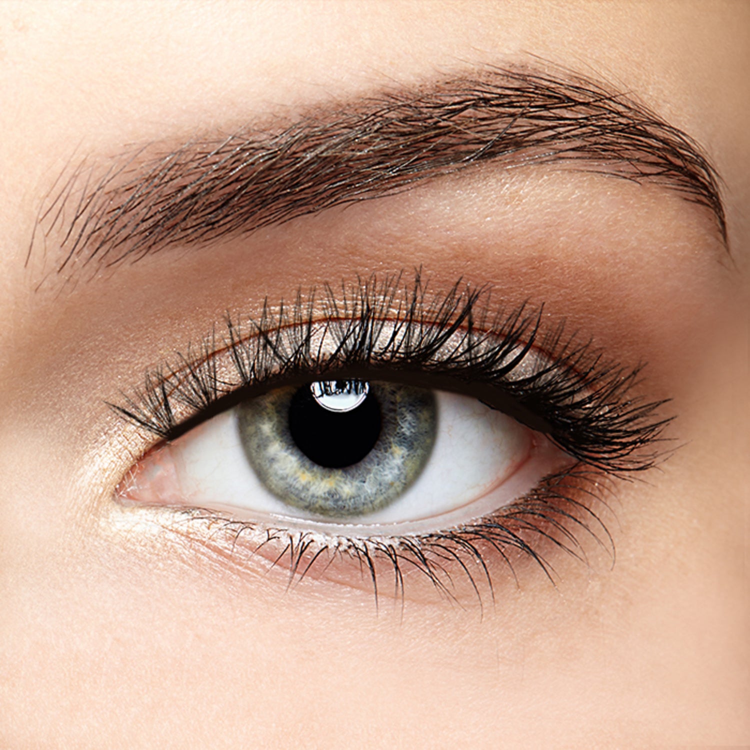 Close-up of a light blue eye with long, curled black faux lash extensions on the upper eyelid, featuring natural-looking volume and length.