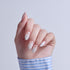 Hand displaying almond-shaped nails with white polish and shell design details.