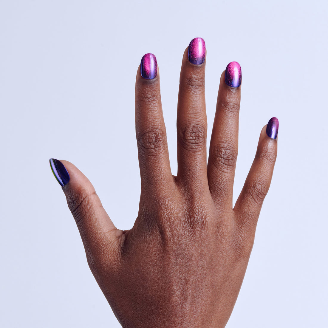 Hand displaying metallic purple and blue chrome nail polish against white background.