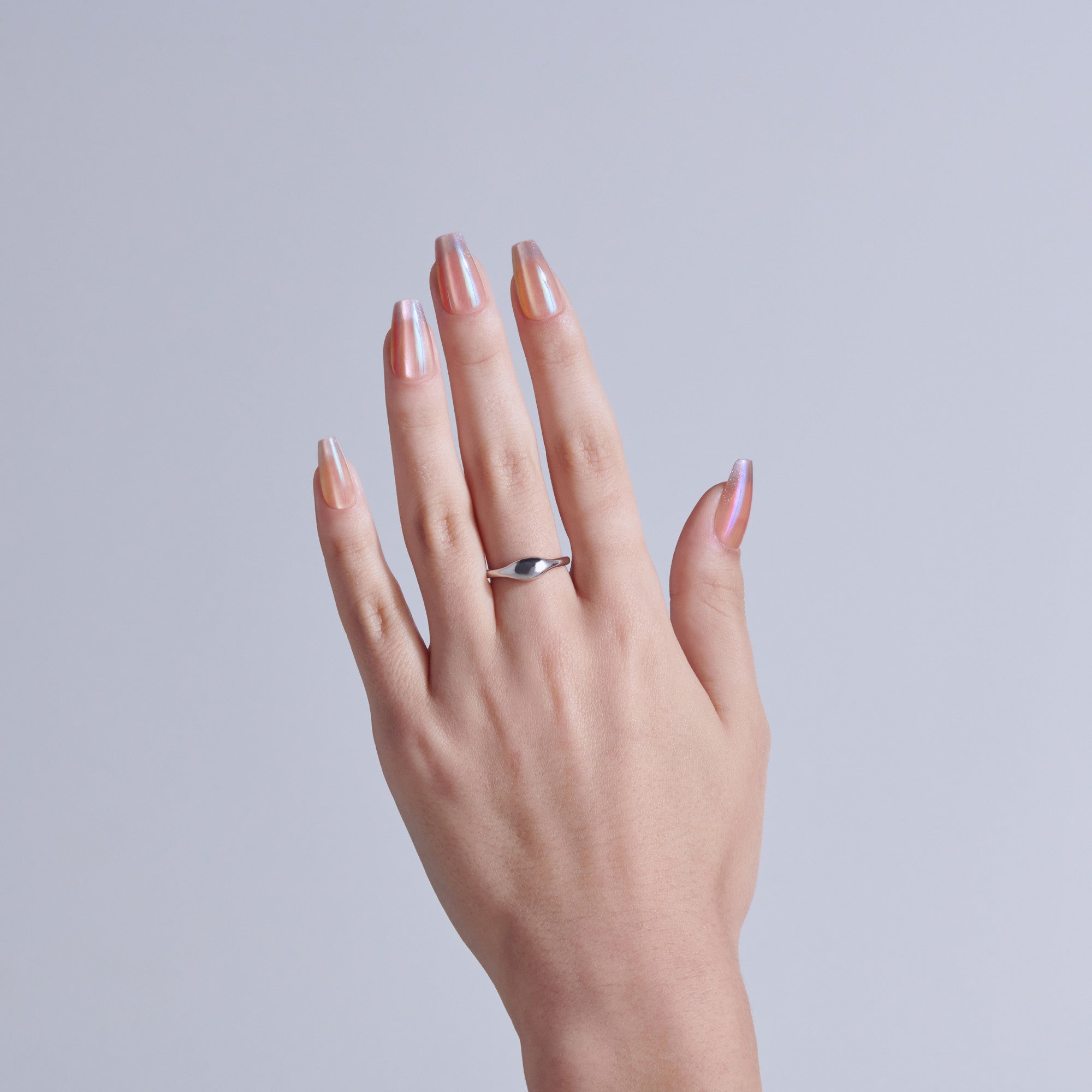 Hand displaying pink metallic nail polish and silver ring against white background.