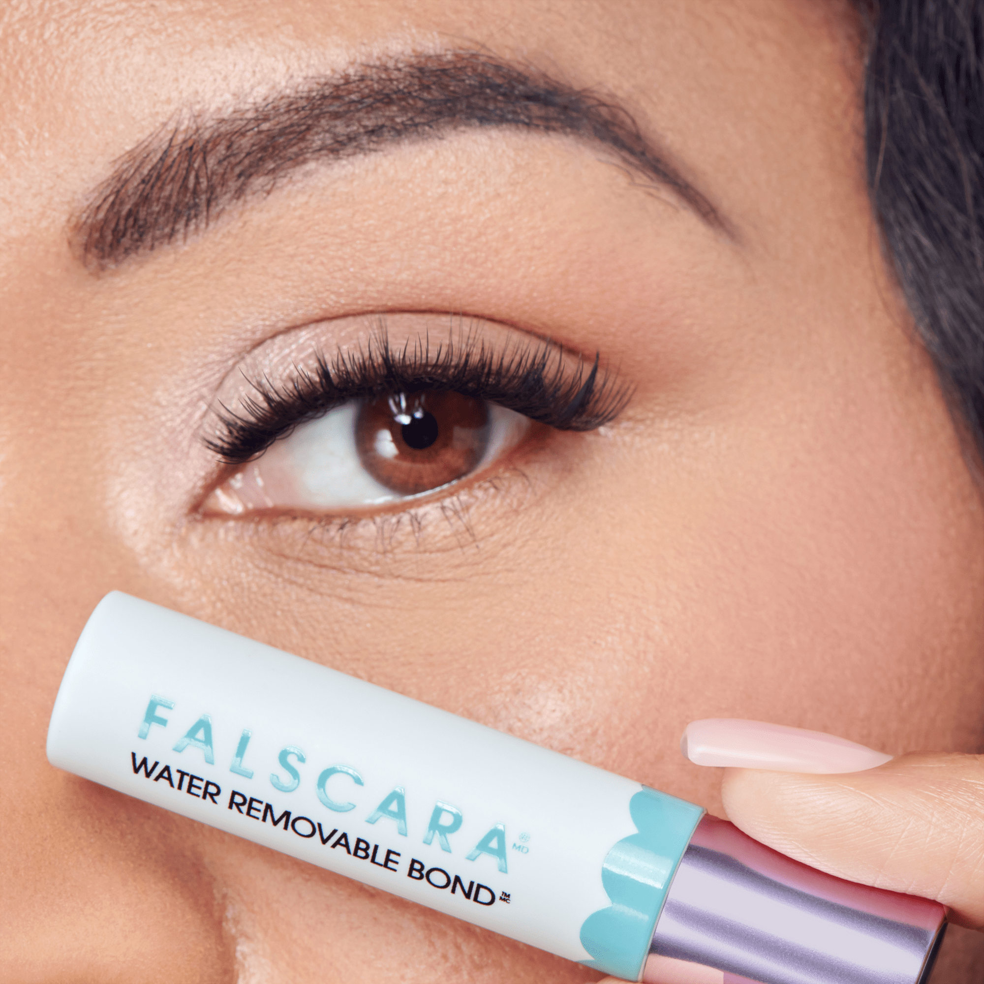 Close-up of eye with false lashes next to Falsara Water Removable Bond mascara tube