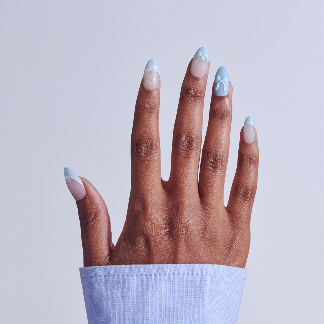 Hand with ombré nail art featuring blue tips and geometric white patterns on natural nails.