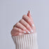 Manicured hand with white-tipped French nails wearing cream sweater and gold ring.