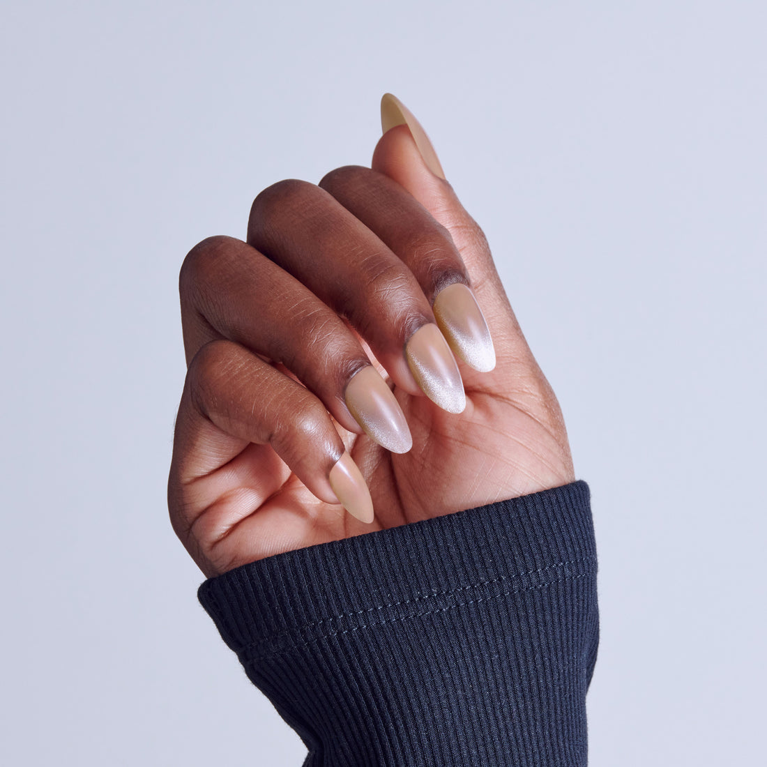 Close-up of hand with almond-shaped nails featuring nude and white ombre nail polish design.