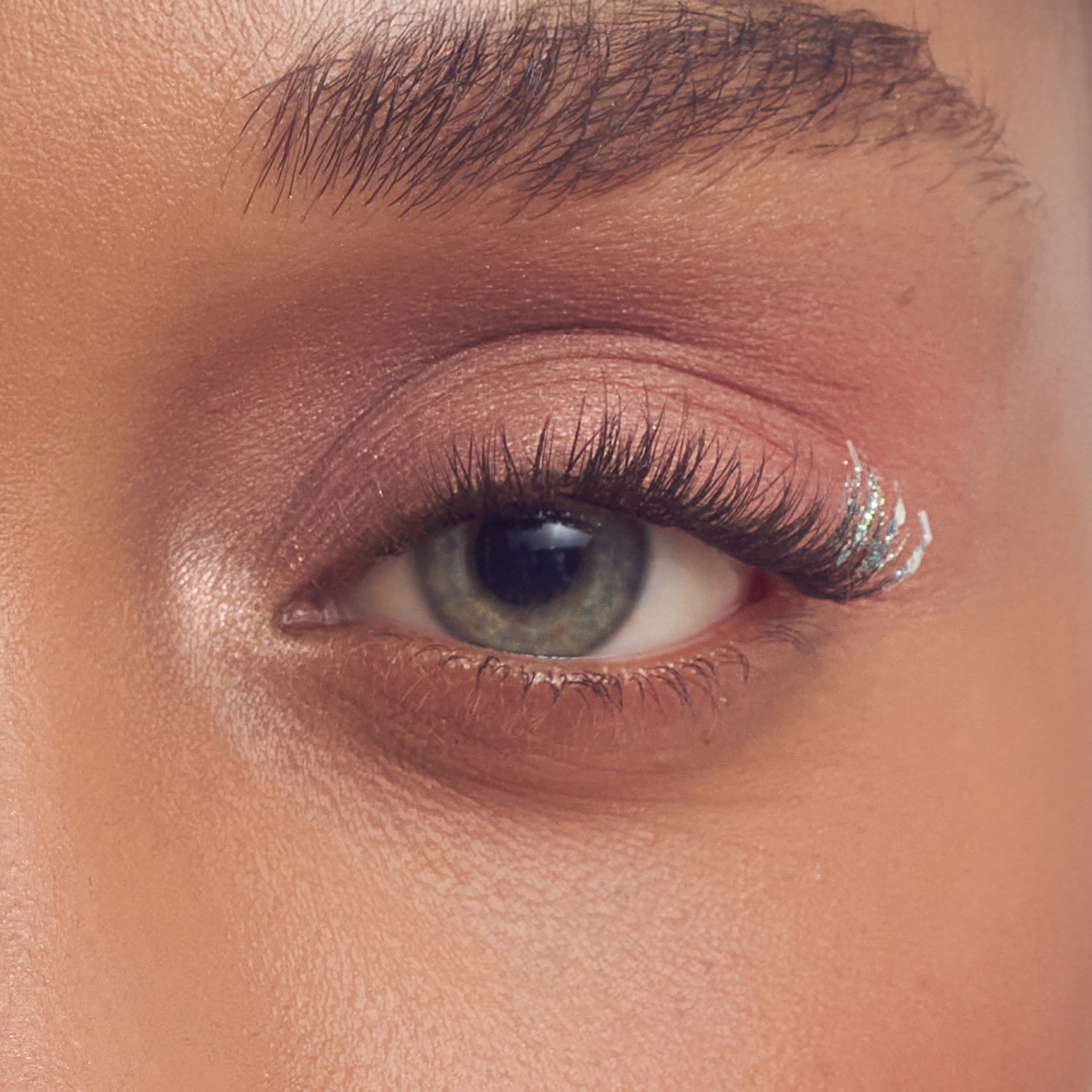 Close-up of eye with warm brown eyeshadow, dark eyeliner, and volumized lashes with glitter accent.