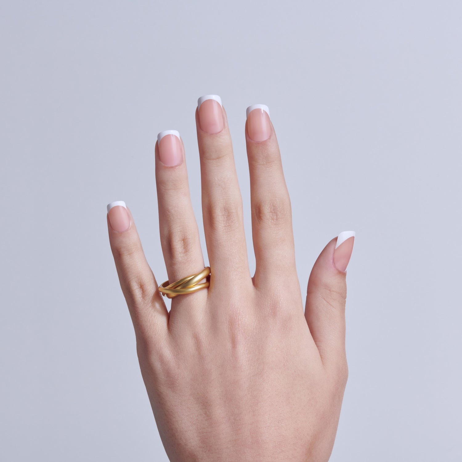 Hand displaying classic white French manicure with gold band ring on light background.