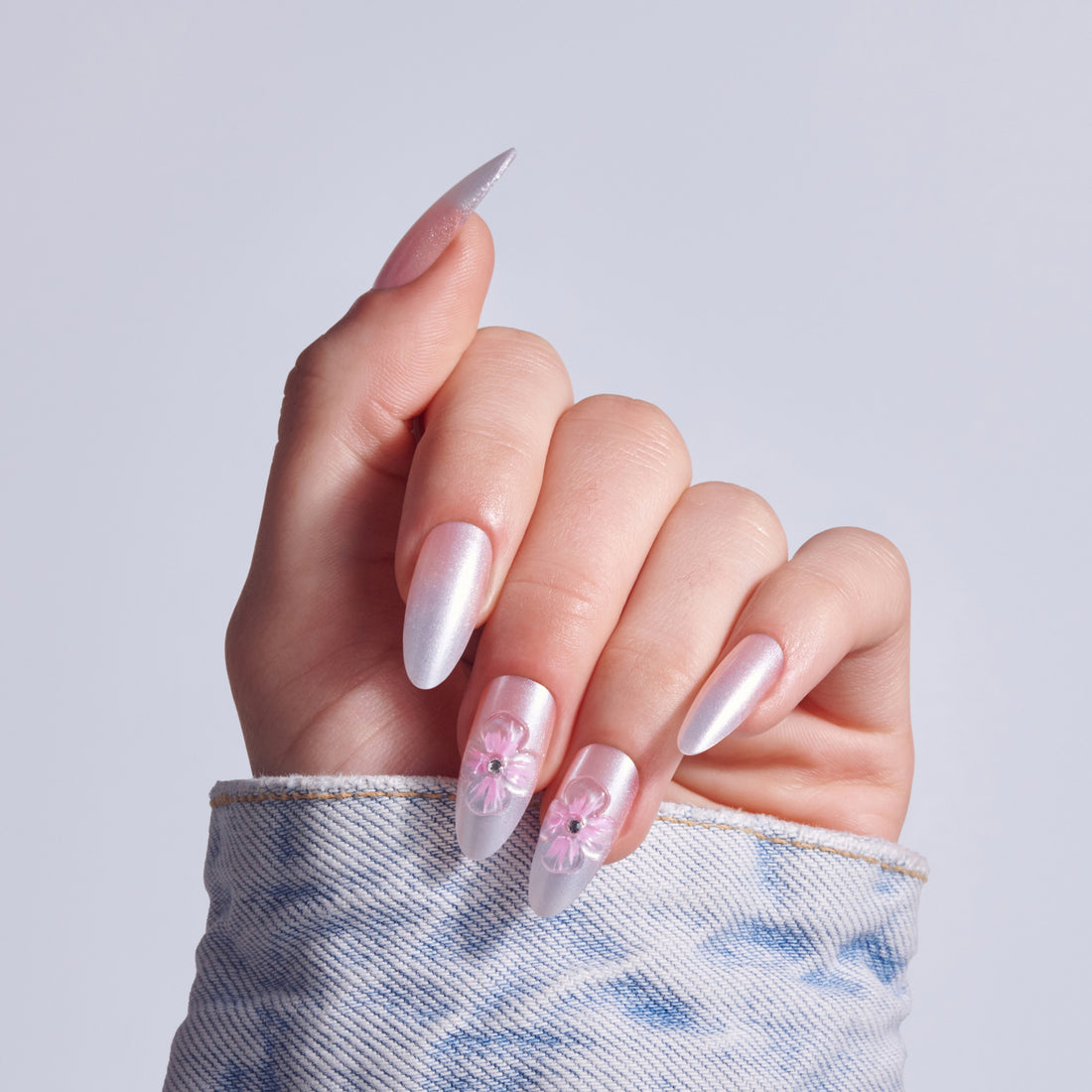Manicured hand displaying almond nails with pink pearl polish and floral nail art designs.