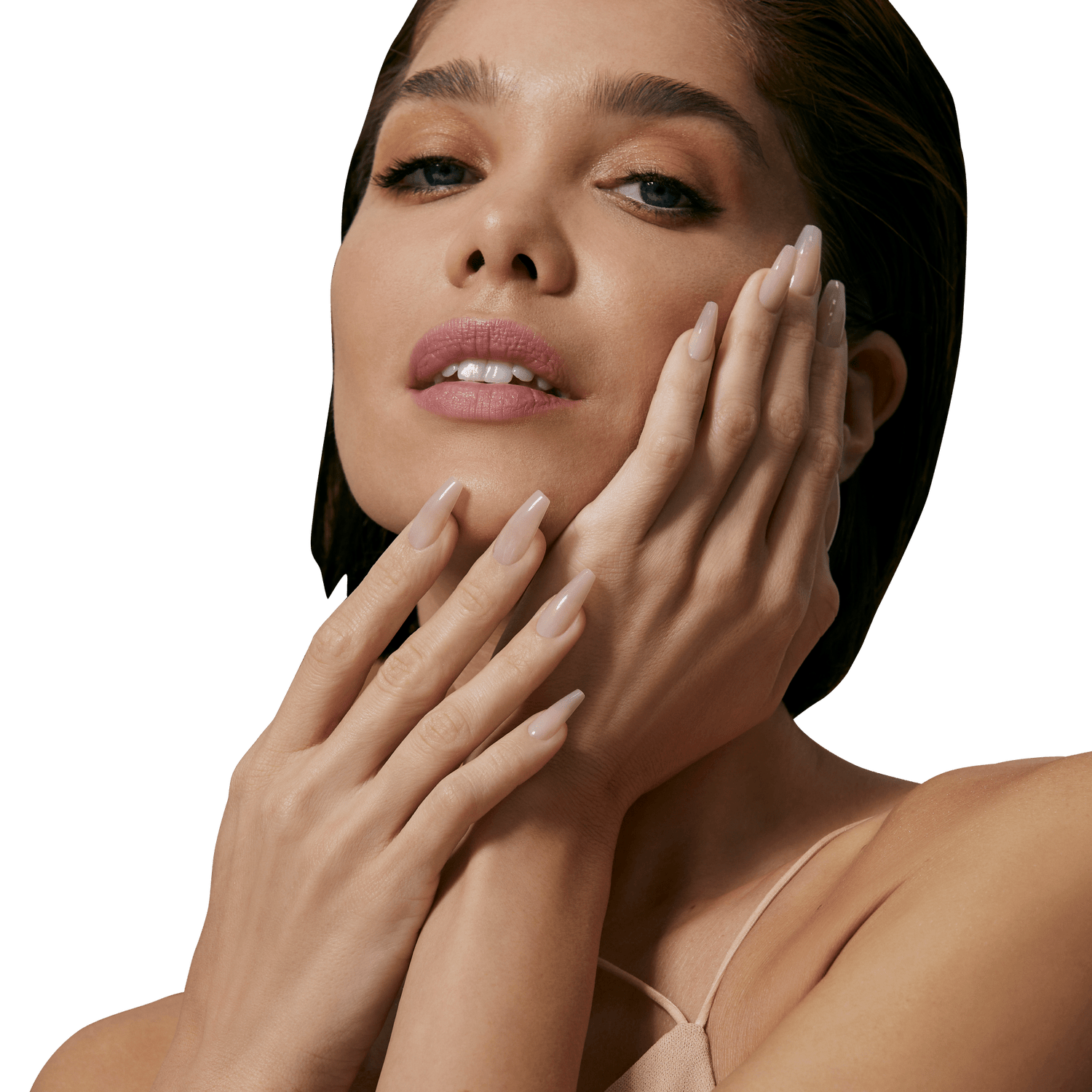 Close-up of a woman with light nude, glossy press-on nails shaped in a long coffin style, gently touching her face and neck, wearing a beige strap top.