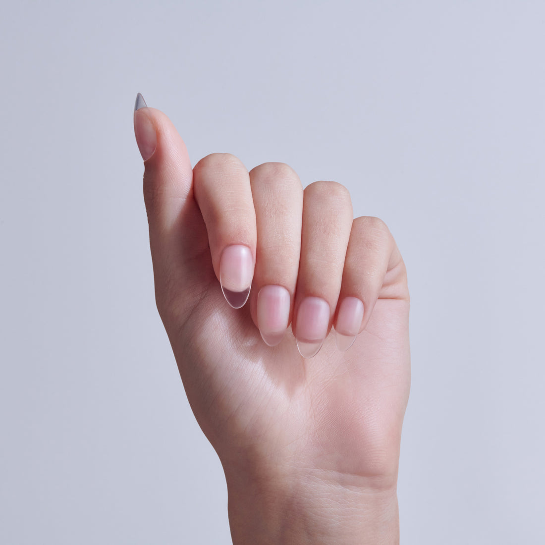 Hand displaying almond-shaped nails with soft pink nail polish on light background.