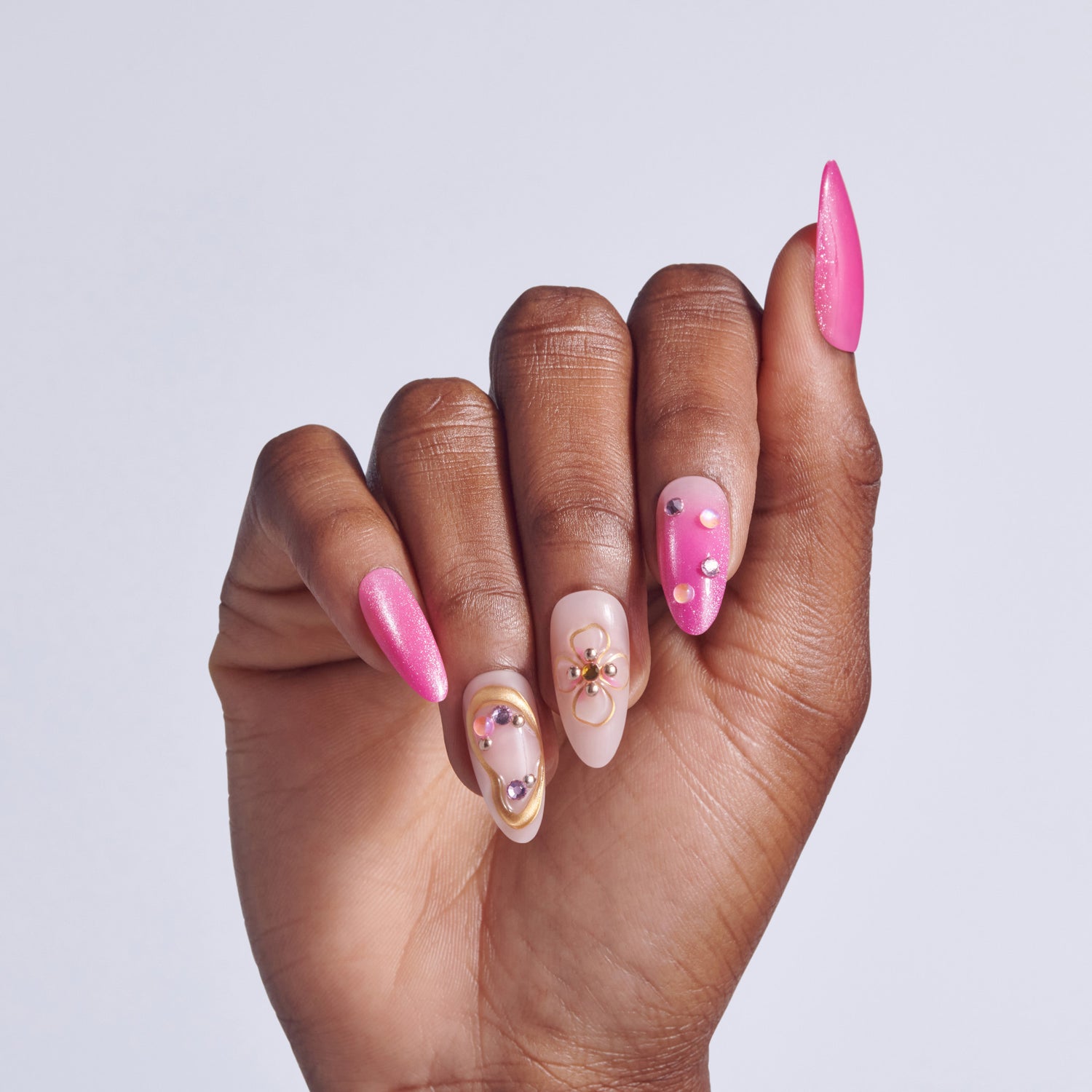 Hand displaying almond nails with hot pink glitter and nude designs featuring rhinestone accents.