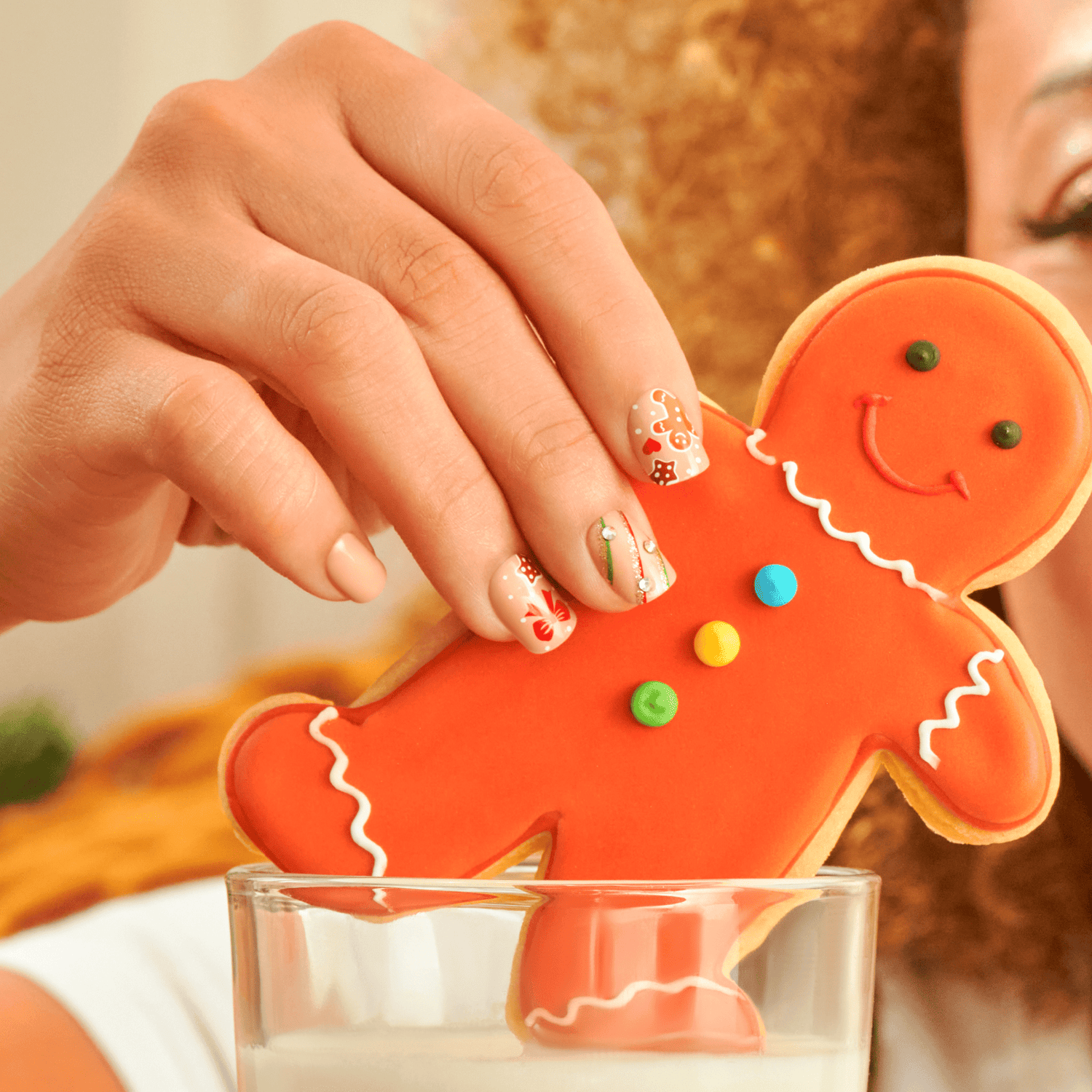 Hand holding decorated gingerbread man cookie over milk glass, festive holiday nail art visible.