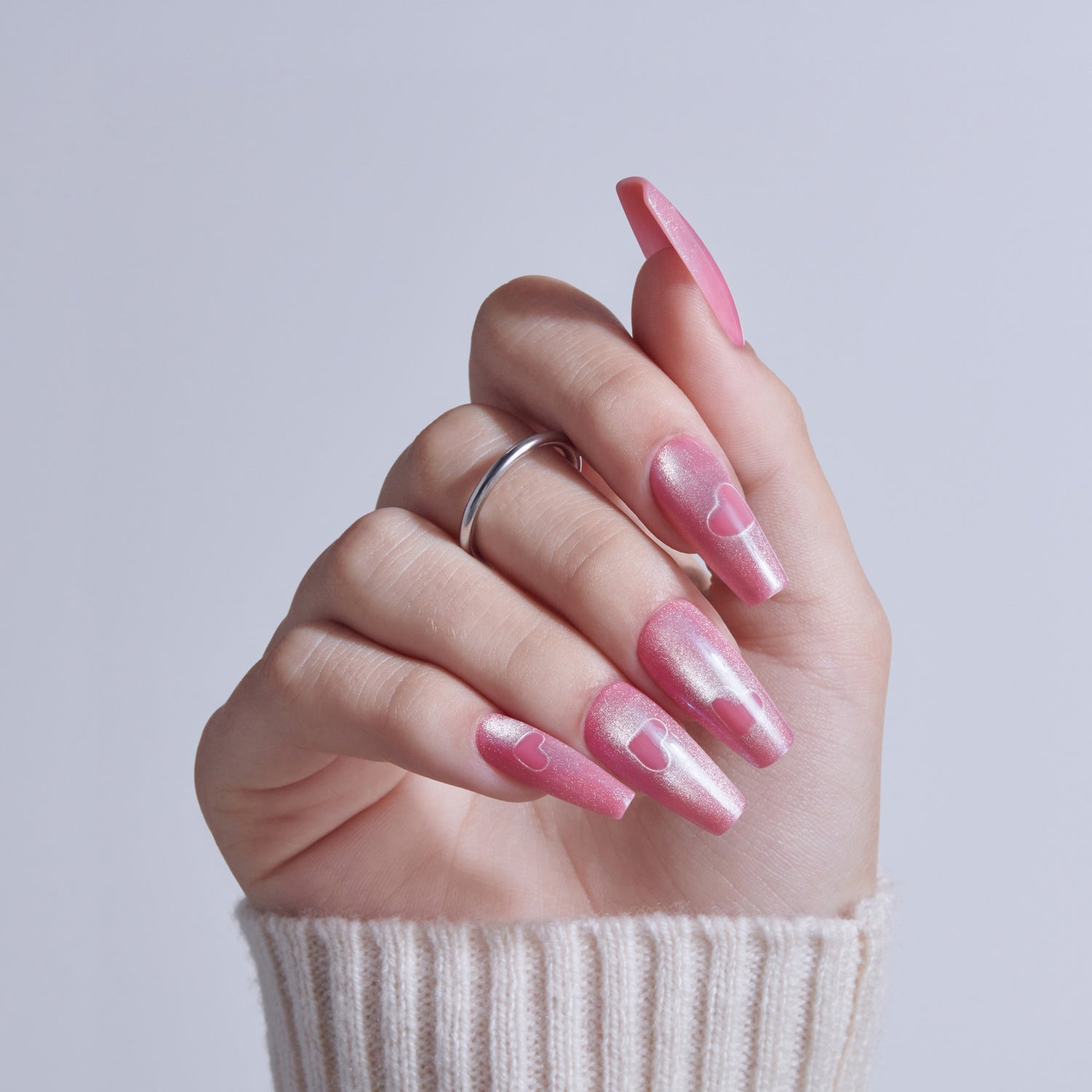Hand with pink glittery coffin nails and heart designs, wearing silver ring