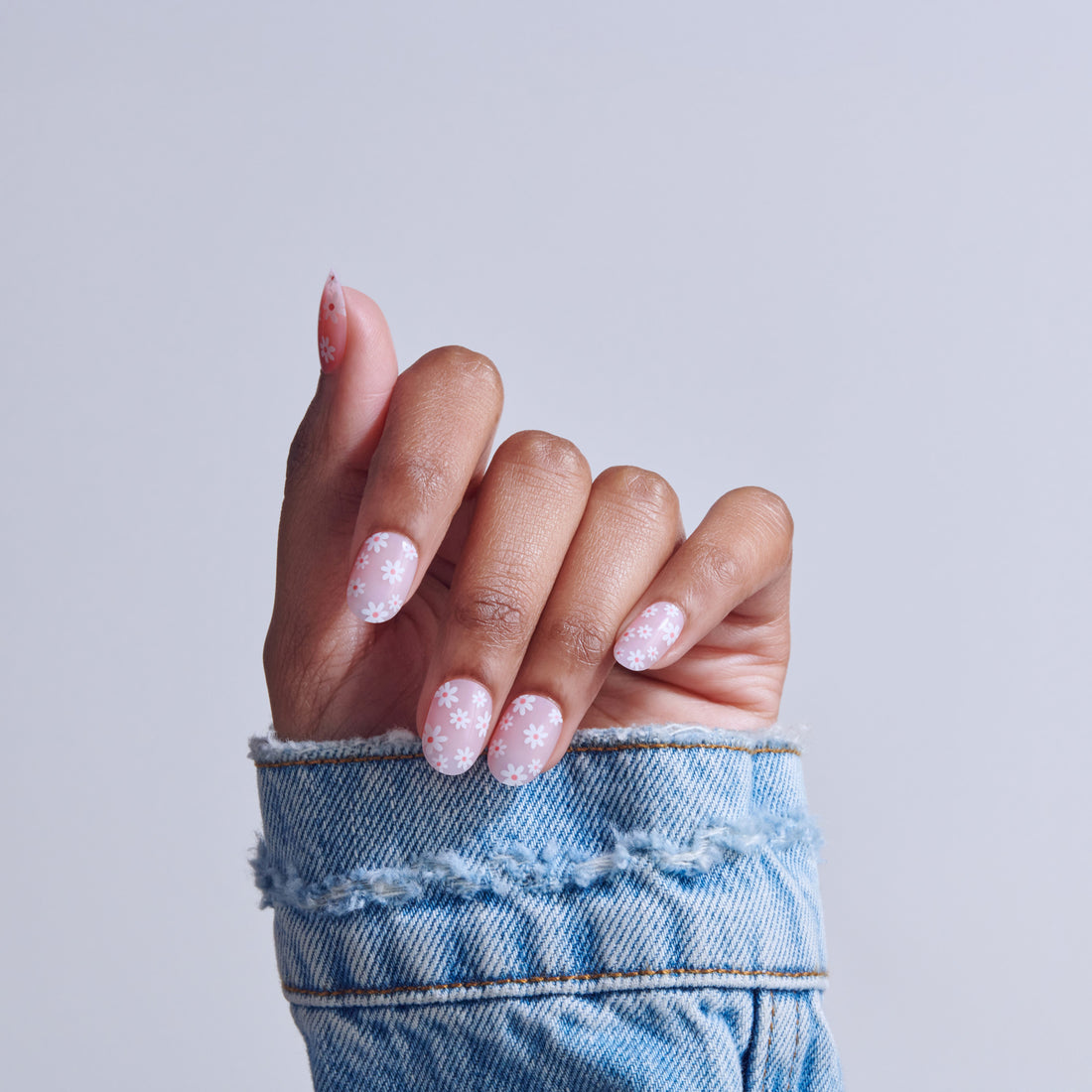 Hand with pink snowflake nail art design against light blue background