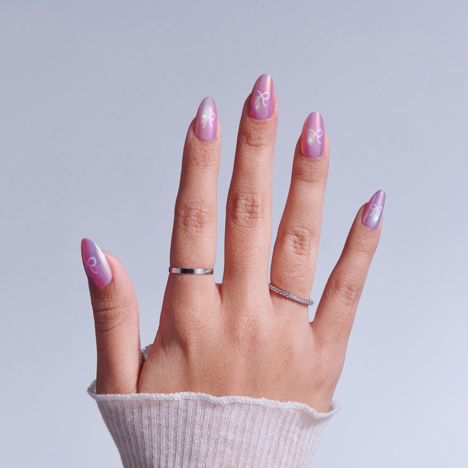 Hand with pink ombre nails featuring white symbol designs and silver rings against light background