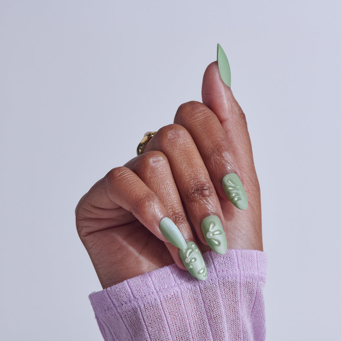 Hand with almond nails featuring sage green and white nail art with leaf designs, wearing lavender sleeve.