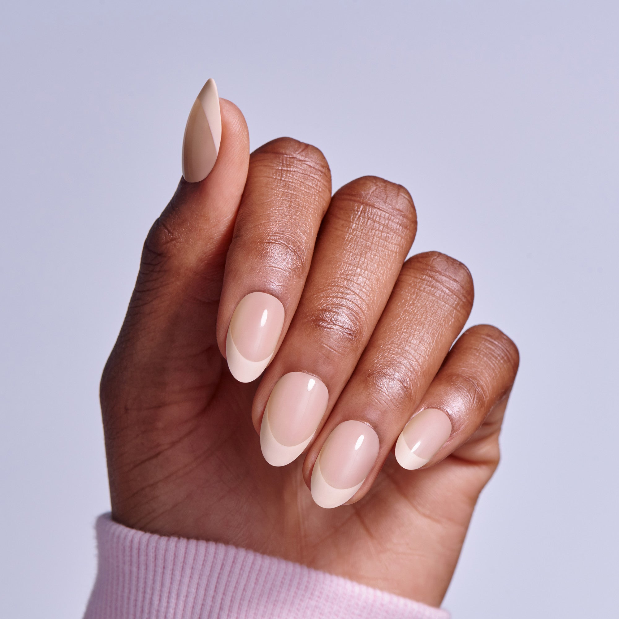 Close-up of hand displaying nude and white ombre acrylic nails against light background.