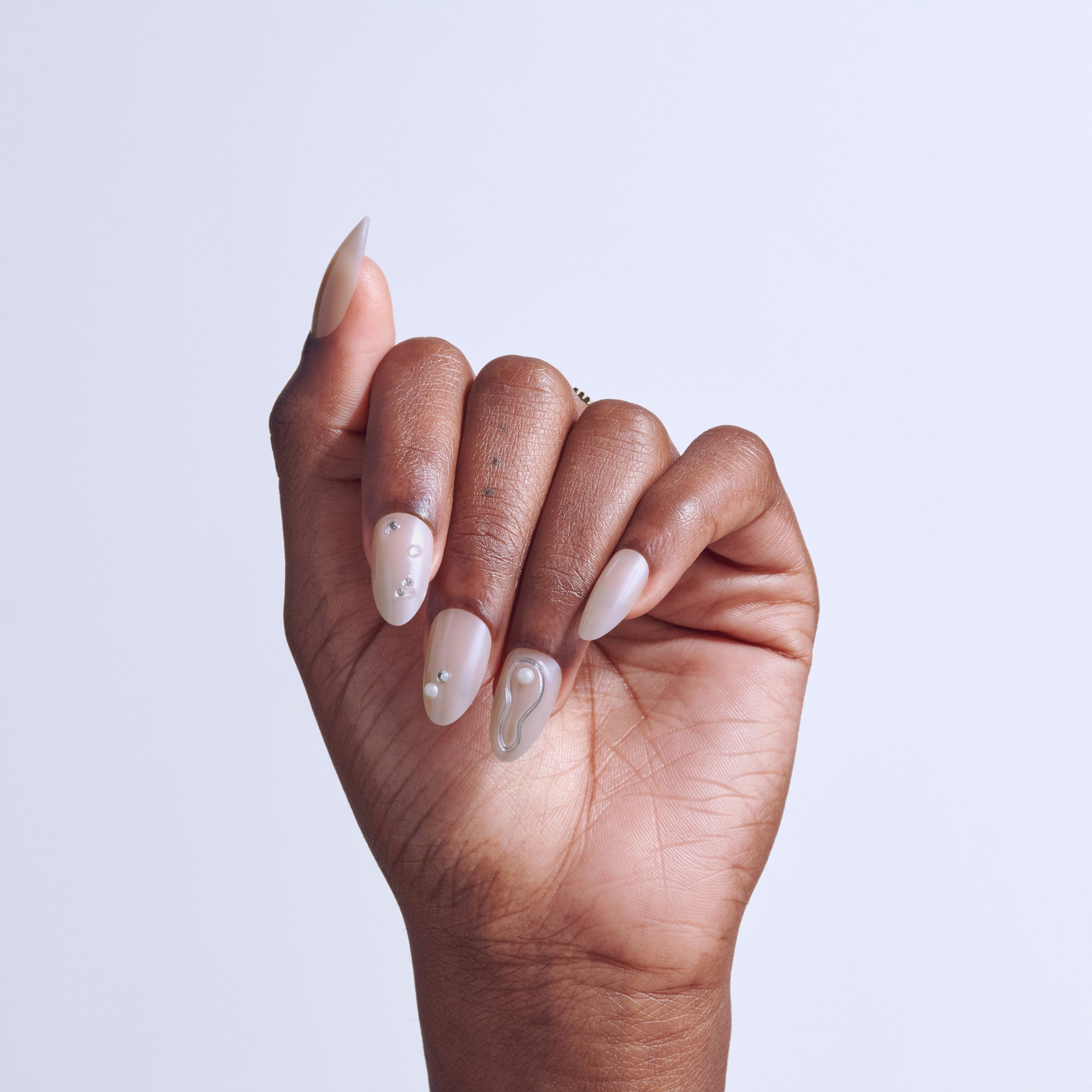 Hand displaying nude and sheer nail polish with rhinestone accents on almond-shaped nails.